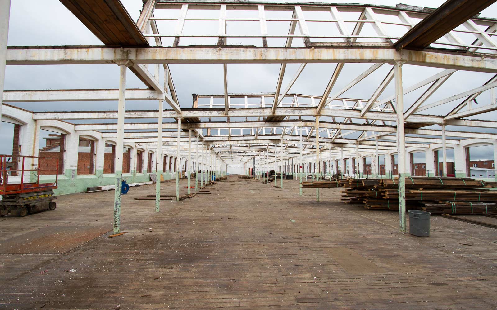 Third floor of old mill building, the roof has been removed leaving behind the wooden beam structure and the exterior brick walls on the left and right side. The wooden beams will be dismantled and carefully stacked.