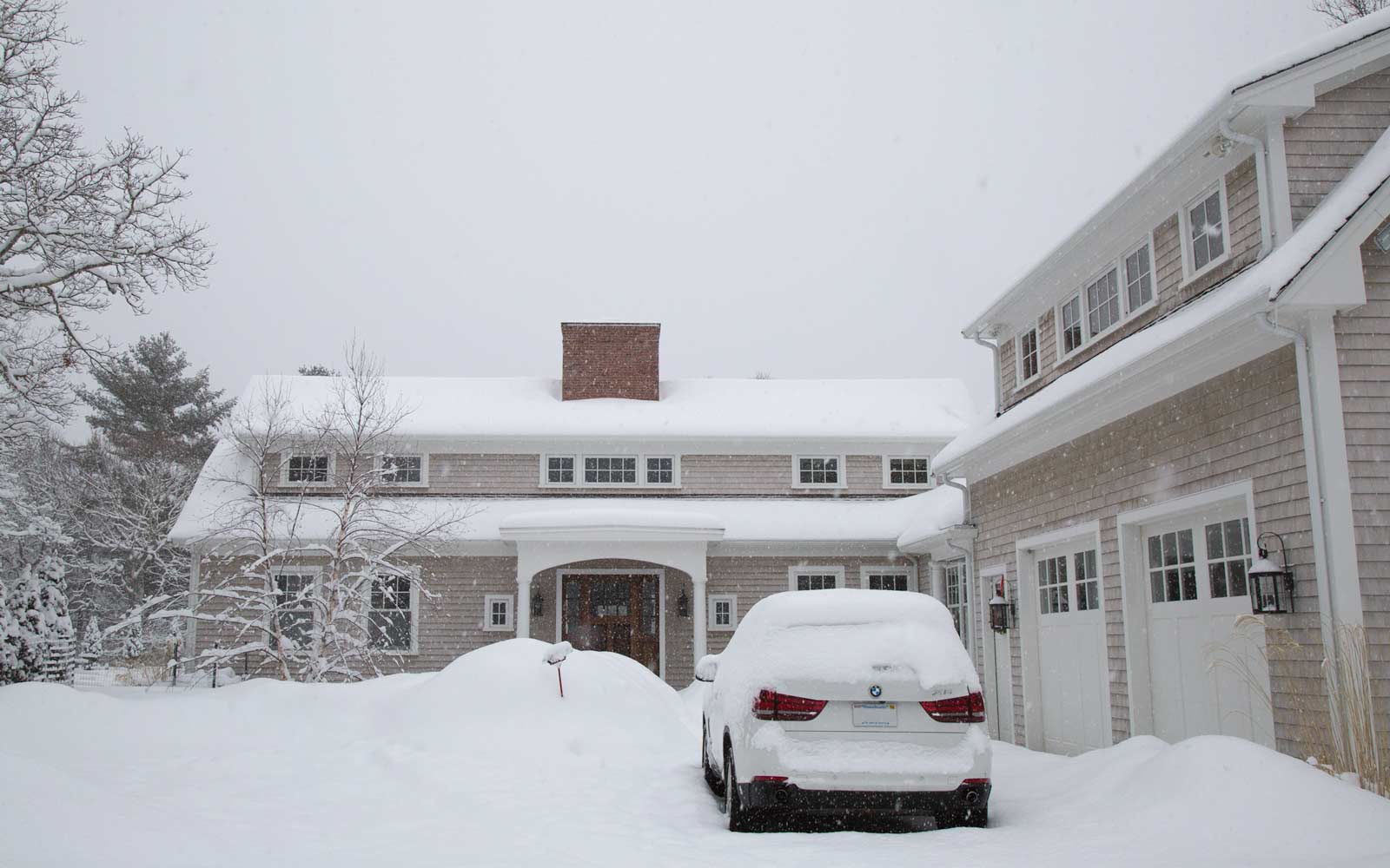 house during snow storm, bmw parked in drive way and brick reclaimed brick chimney on roof of house.