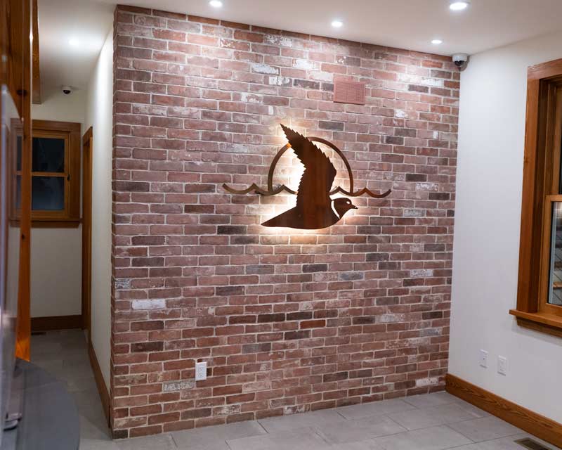 Completed reclaimed brick wall inside customers retail store lobby. Metal sign logo is mounted to the wall and led backlit.