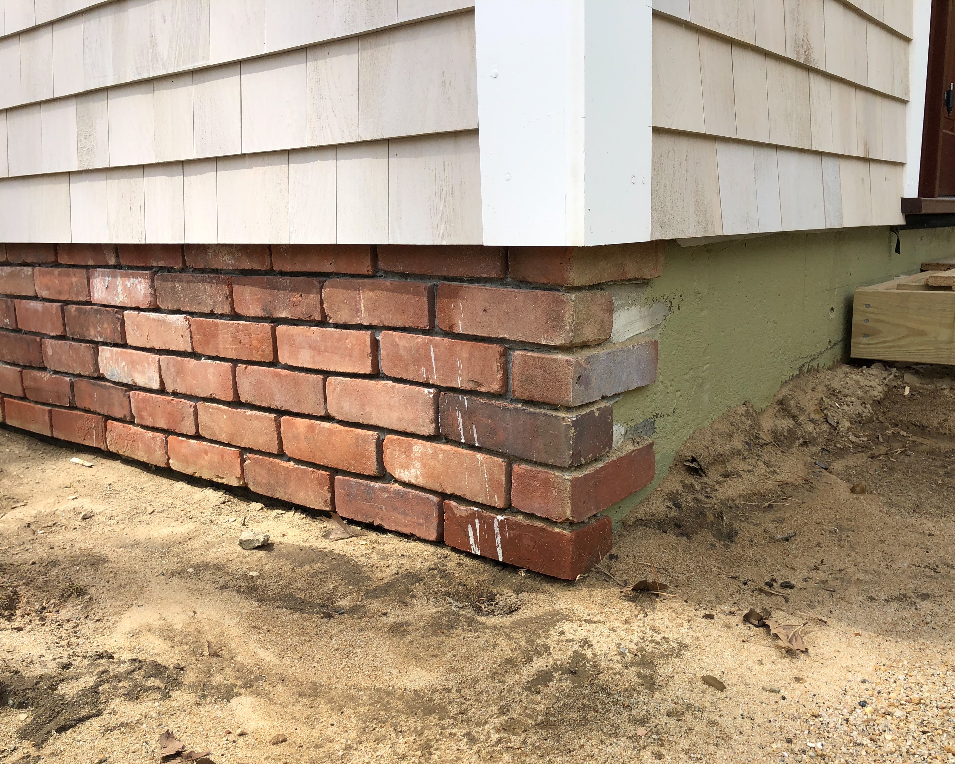 Exposed house cement foundation covered with reclaimed brick tiles. In progress, you can see the L shaped brick tiles taking a 90 degree turn.